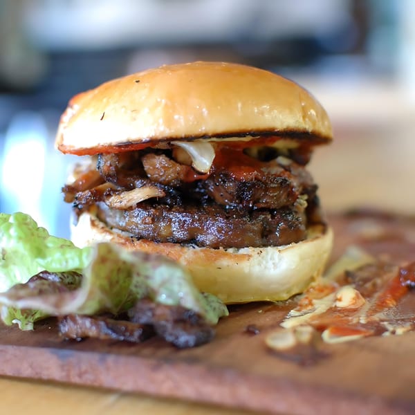 Close-up of a vegan burger with two patties, mushrooms, and lettuce on a wooden board.