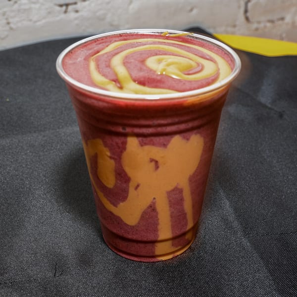 Essential Smoothies Cafe's vegan smoothie, a vibrant swirl of red and yellow, in a clear cup.