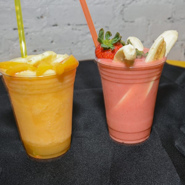 Two vegan smoothies, one orange with mango, one pink with strawberry and banana, on a black surface.