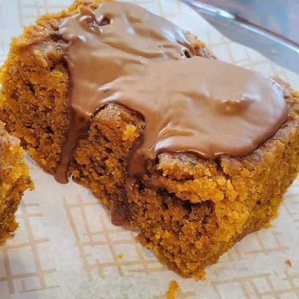 A vegan pumpkin spice bar with chocolate frosting drizzled on top, on a white paper liner.