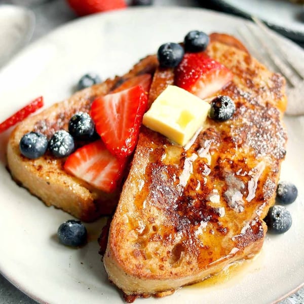 Two slices of vegan French toast topped with fresh strawberries, blueberries, and a pat of butter.