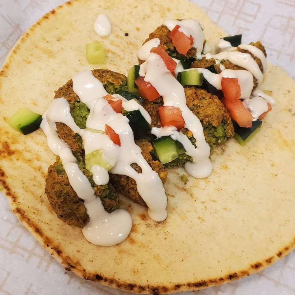 Vegan falafel wrap with white sauce, diced tomatoes, and cucumbers on a flatbread.
