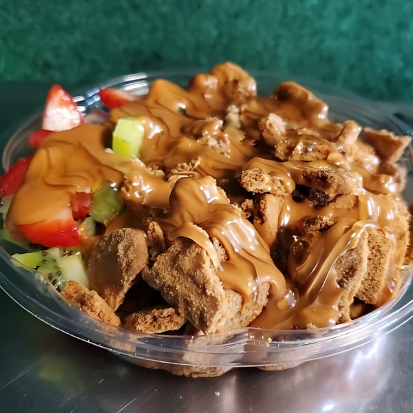 Vegan dessert with fruit, cookies, and a creamy caramel-colored sauce in a clear plastic bowl.