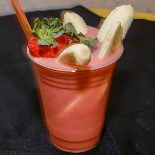 Strawberry banana smoothie in a clear cup with fresh strawberry and banana slices on top.