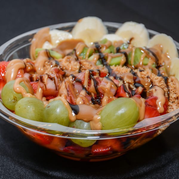 A vibrant vegan fruit bowl with grapes, strawberries, kiwi, bananas, peanut butter, and chocolate drizzle.